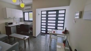 Un espacio habitable compacto con kitchenette, comedor y un ventanal grande.