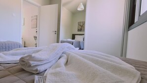 Un dormitorio con dos camas, una colcha blanca en una de ellas, y una puerta que da a otra habitación.
