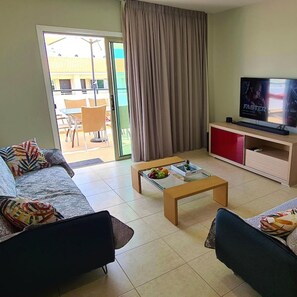A living room with a sofa, a coffee table with fruit, a TV, and a sliding glass door to an outdoor area. - 36 KAP - Horizon Apartment (Paralimni)