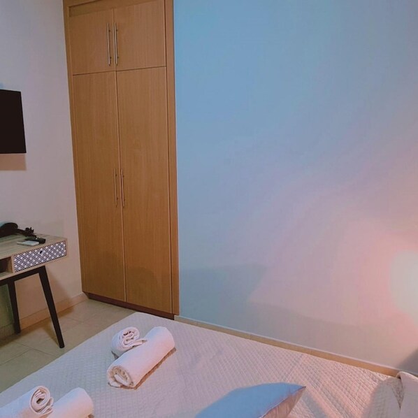 A bedroom with a bed, a wooden wardrobe, a small table with a patterned tablecloth, and a wall-mounted TV. - 36 KAP - Horizon Apartment (Paralimni)