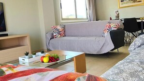 Ett modernt vardagsrum med en grå soffa, ett soffbord med frukt, en tv och en matplats med ett bord och stolar.