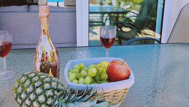 A table with a fruit bowl containing grapes and an apple, a bottle, and two glasses of red wine. - 51 PER - Sunny Bay Villa (Paralimni)
