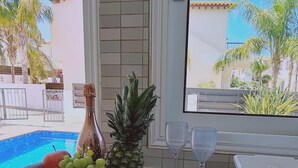 A kitchen counter with a fruit basket, a pineapple, a bottle, and two wine glasses. - 51 PER - Sunny Bay Villa (Paralimni)