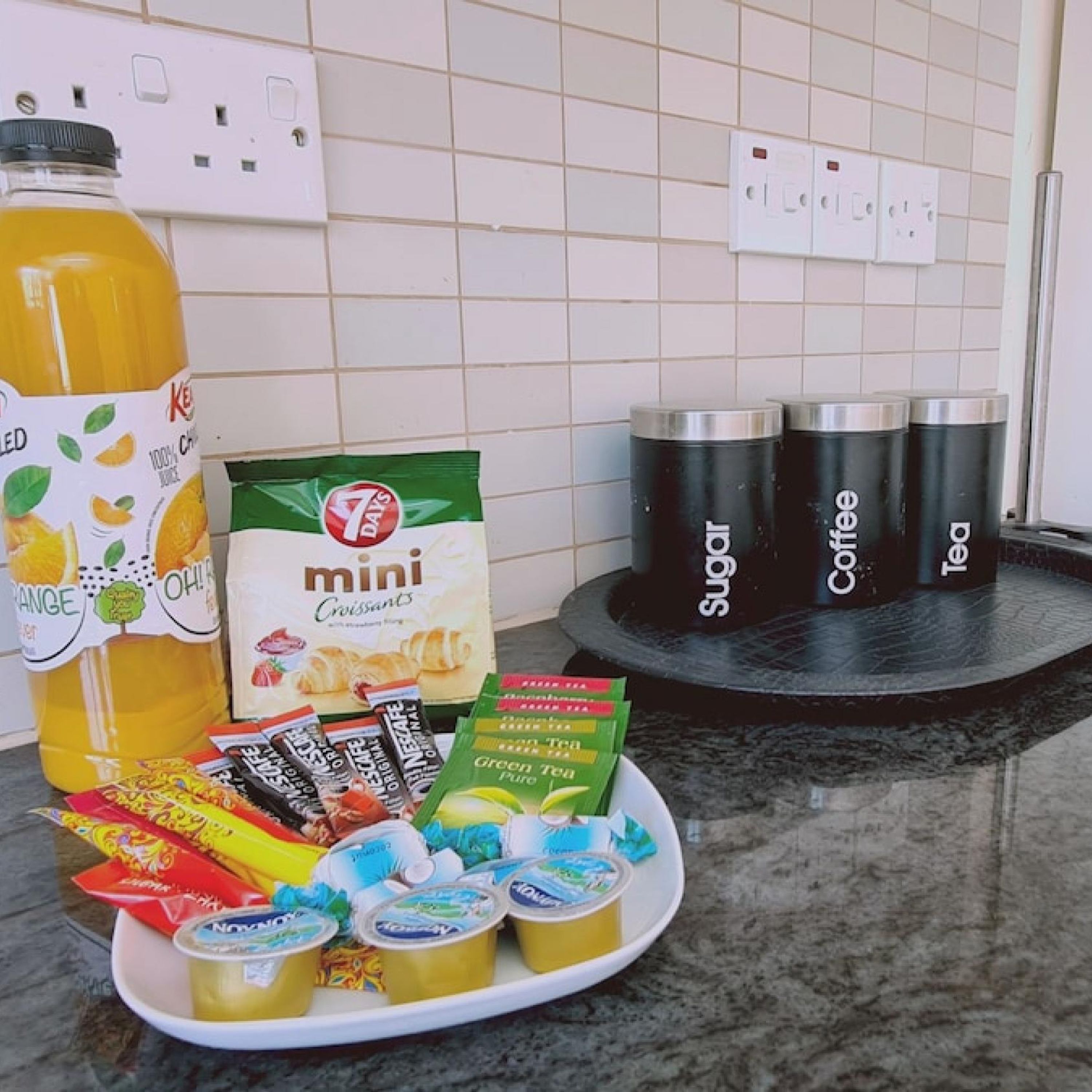 A kitchen counter with a bottle of orange juice, a box of mini croissants, and various tea and coffee products.