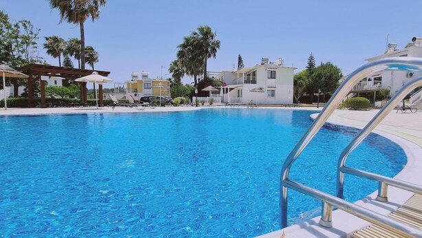 A clear blue swimming pool with a metal ladder, surrounded by palm trees and modern buildings. - 42 PRO -stay Symphony Apartment (Paralimni)