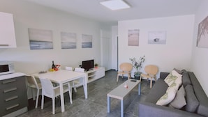 A modern living room with a sofa, a dining table, and chairs. There are wall art pieces and a flat-screen TV. - 14 AN - 114 Nissi Twins Apartment (Ayia Napa)