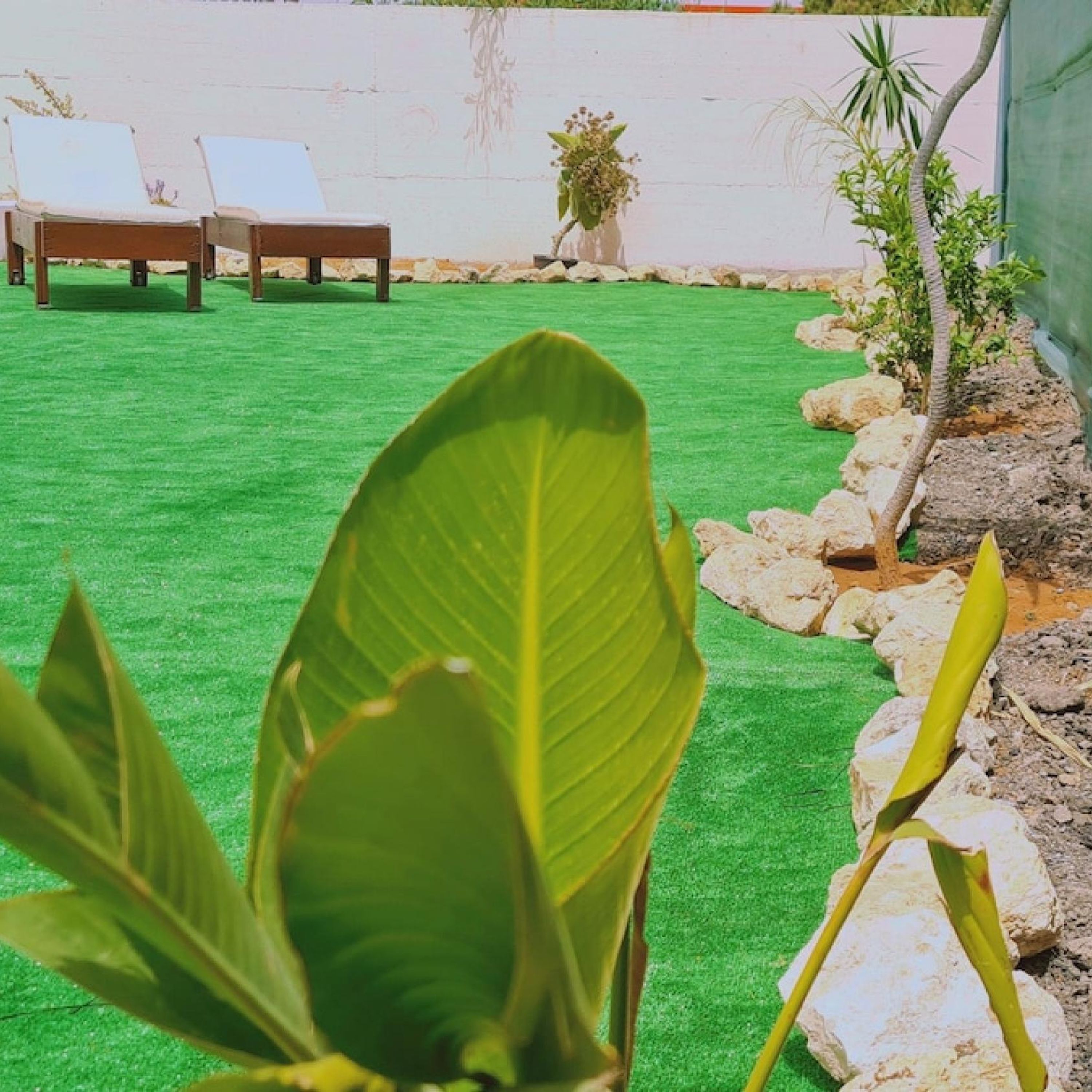 Un jardín con césped artificial, algunas sillas de descanso y un pequeño jardín de rocas.