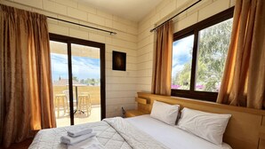 A hotel room with a large bed, a wooden headboard, and a view of the outdoors through a window. - 25 AN - Pernera House (Ayia Napa)