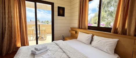 A hotel room with a large bed, a wooden headboard, and a view of the outdoors through a window.