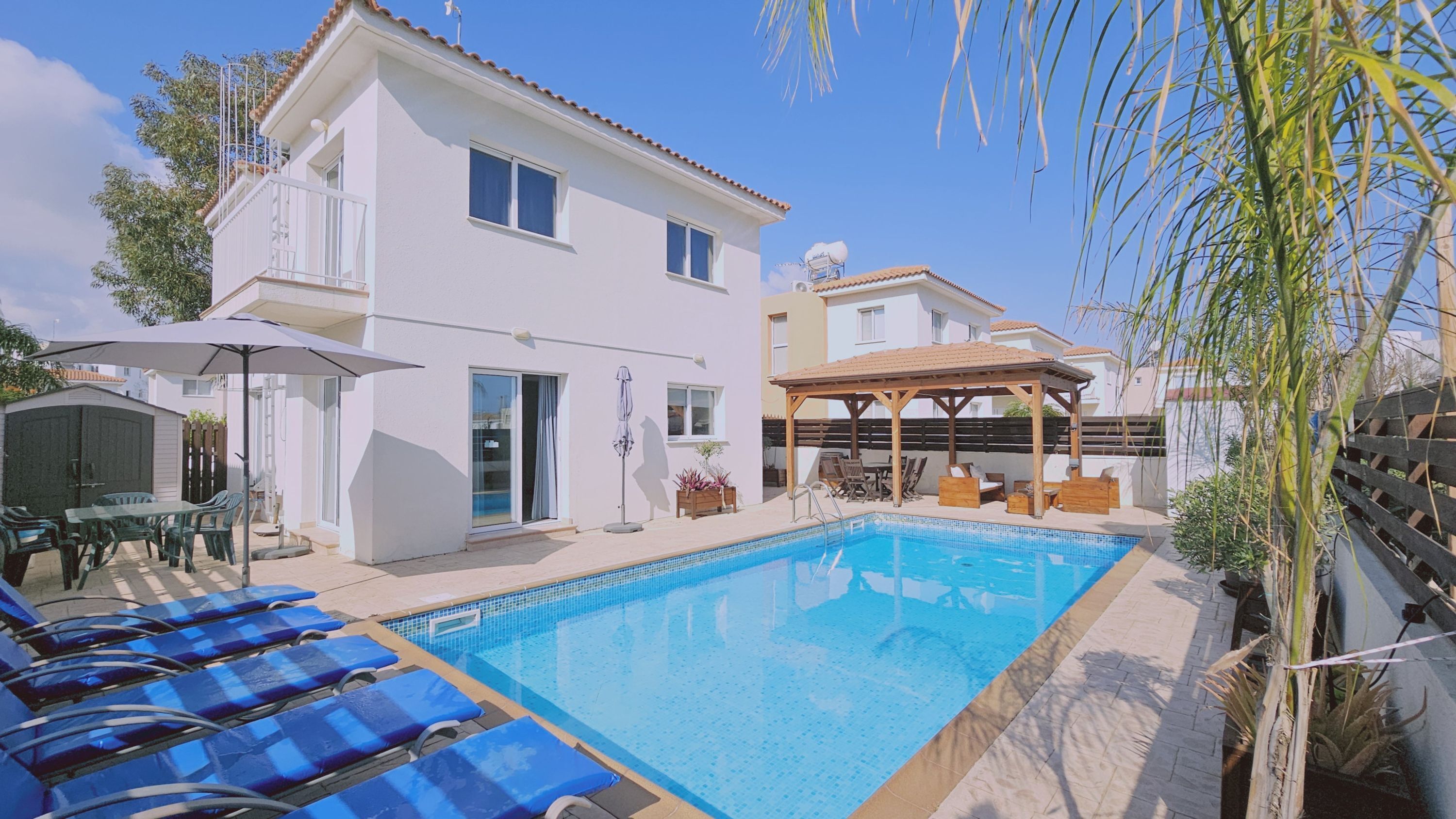Ein zweistöckiges Haus mit Swimmingpool, Sitzgelegenheiten im Freien und einer überdachten Terrasse.