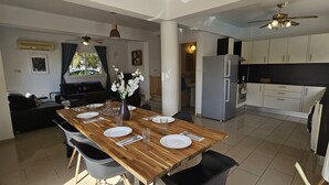 A modern kitchen with a refrigerator, oven, and dining area with a wooden table set for four. - 08 PER - Villa Anemone (Paralimni)