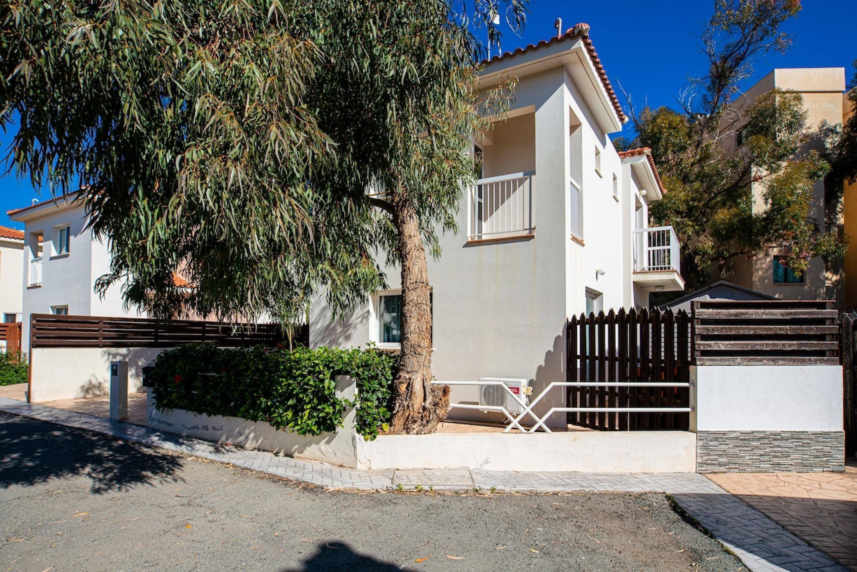 A two-story residential building with a balcony, a gated entrance, and a tree in front.