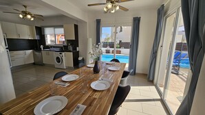 A modern kitchen with a dining area, a washing machine, and a view of a swimming pool. - 08 PER - Villa Anemone (Paralimni)