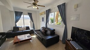 A modern living room with a sofa set, a coffee table, a TV, and a ceiling fan. - 08 PER - Villa Anemone (Paralimni)