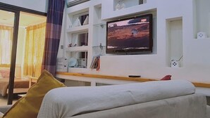 Ett modernt vardagsrum med en stor platt-TV som är monterad på väggen, en soffa med kuddar och en glasdörr som leder till ett annat rum.