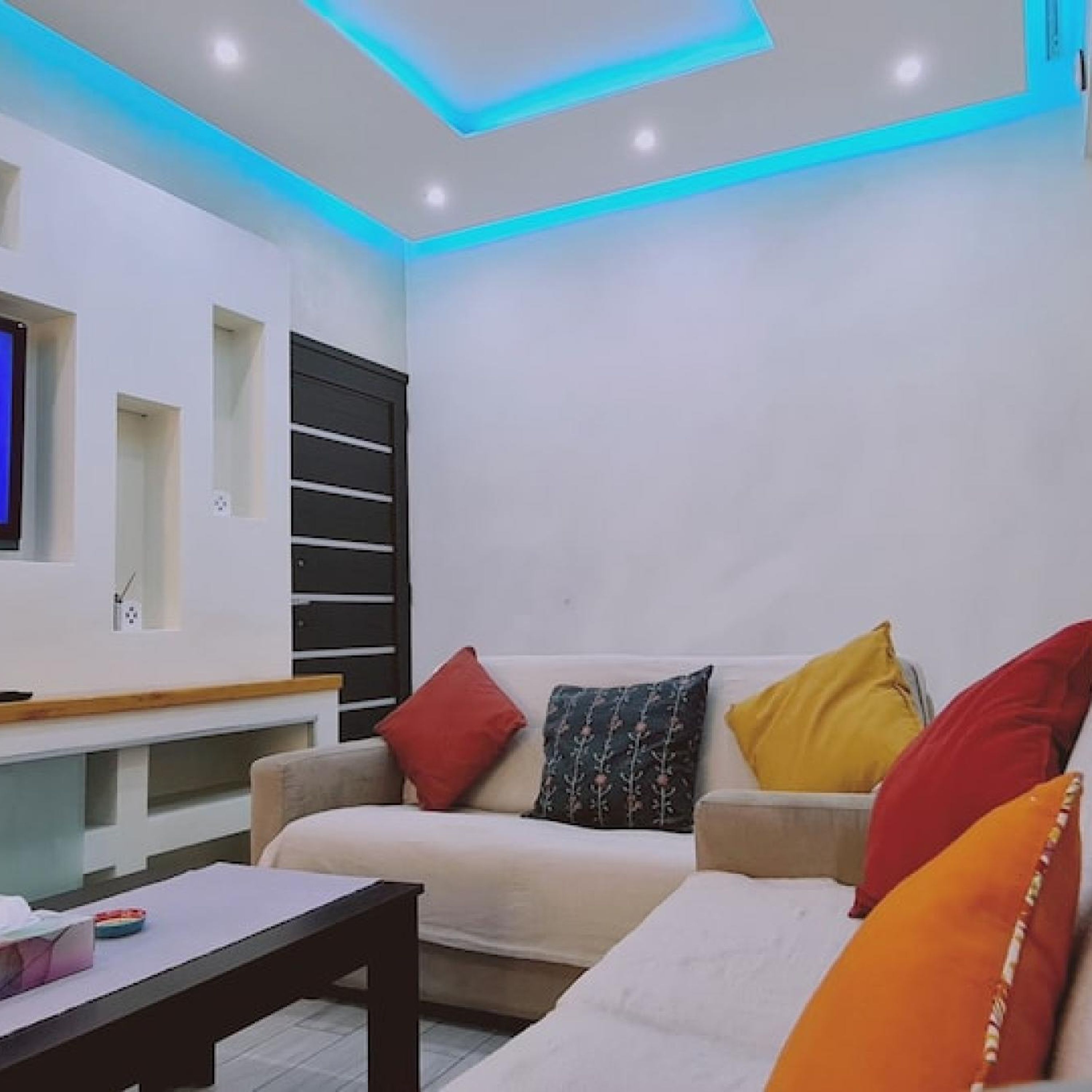A modern living room with a sofa, colorful cushions, a coffee table, and a TV mounted on the wall.