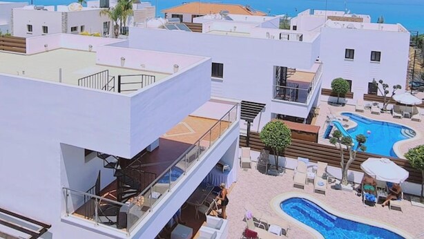 Un moderno resort con piscina en la azotea, cielo azul despejado y vistas al océano.