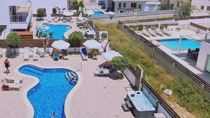 Zona de piscina en la azotea con varias piscinas, sillas de descanso y sombrillas.