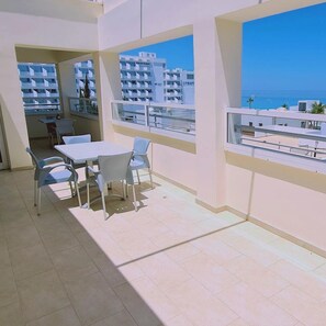 A balcony with a table and chairs, overlooking a coastal area with buildings and the sea. - 40 PRO 1 - Sunrise Beach Apt 1 (Paralimni)