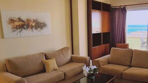 Una sala de estar con un sofá color beige, una mesa de centro y vista al océano a través de una ventana.