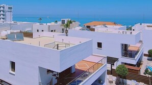 Una zona residencial moderna con edificios blancos, un cielo azul despejado y vista al mar.