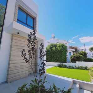 A modern building with a large window, a satellite dish, and a well-maintained lawn. - Stay Sunshine Aura in Protaras (Paralimni)