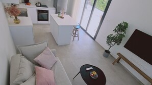 A modern living room with a sofa, a coffee table, a TV, and a kitchen in the background. - Stay Sunshine Aura in Protaras (Paralimni)