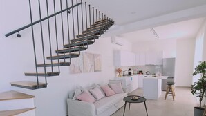 A modern living room with a staircase, a sofa, a coffee table, and a kitchen in the background. - Stay Sunshine Aura in Protaras (Paralimni)