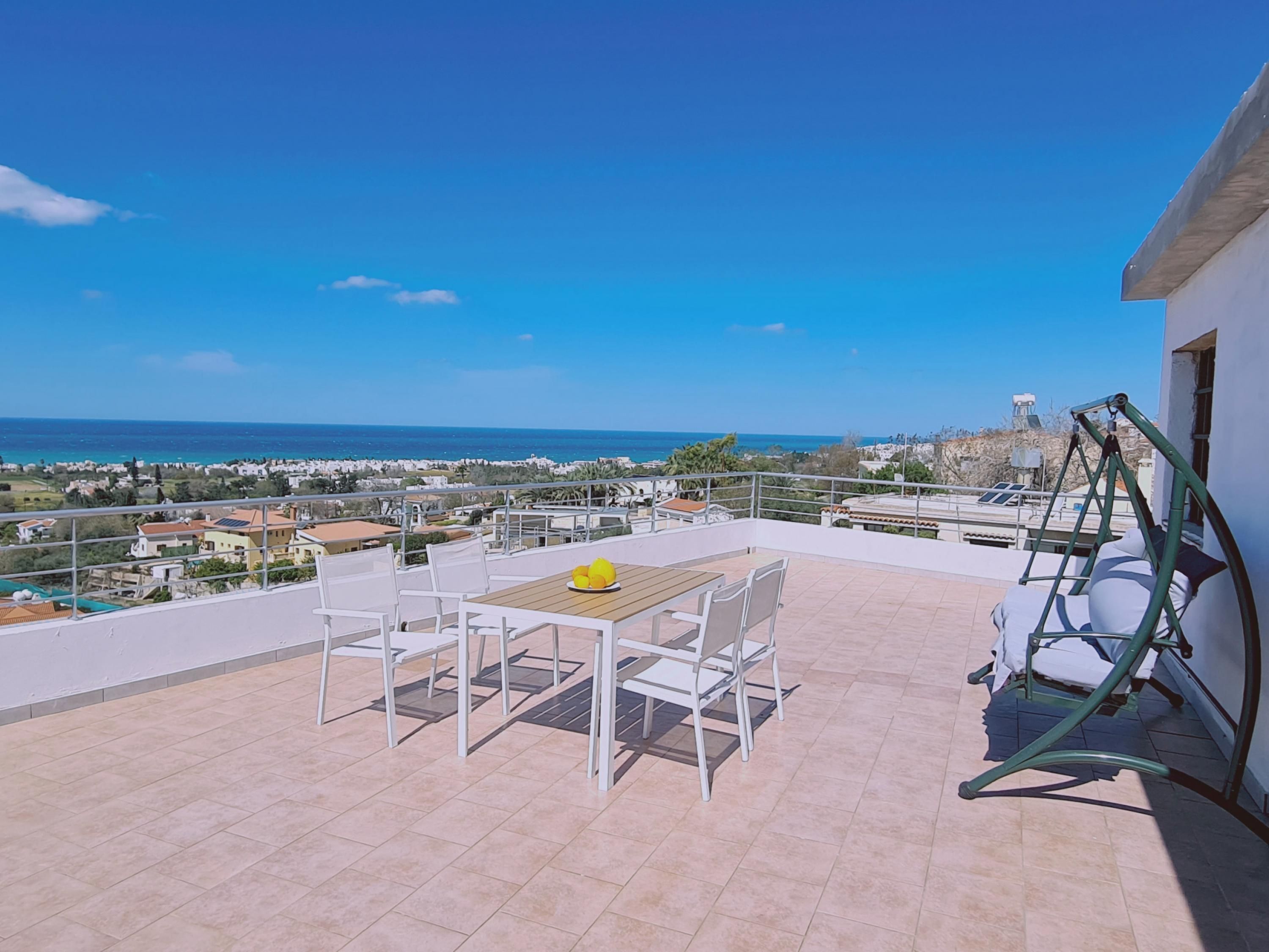 Una terraza con mesa y sillas, con vistas a la costa.
