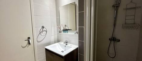 A modern bathroom with a white sink, dark cabinet, and a shower with a handheld showerhead.