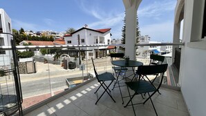 Ein Balkon mit Tisch und Stühlen, der auf eine Straße mit Gebäuden und einem klaren Himmel blickt.