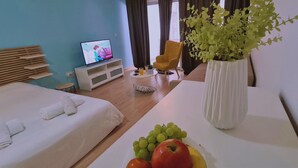 Ett hotellrum med en säng, en tv, en stol, en växt och ett bord med frukt.