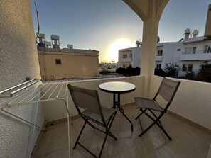 Ein Balkon mit rundem Tisch und zwei Stühlen, mit Blick auf ein Wohngebiet mit Gebäuden und blauem Himmel.