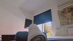 A hotel room with a bed, a window with a view of flowers, a painting on the wall, and an air conditioning unit. - 00 HA - HA DE CO C in Ayia Napa (Ayia Napa)