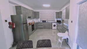 Eine kompakte Küche mit integriertem Waschmaschine, Kühlschrank und Mikrowelle. Es gibt eine kleine Essecke mit zwei Stühlen.