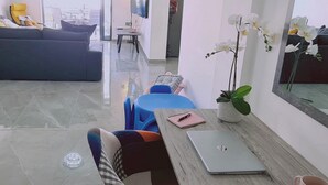 Ein modernes Wohnzimmer mit einer Couch, einem Esstisch mit Stühlen, einem Fernseher und einem großen Fenster.