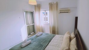 Ein Schlafzimmer mit Bett, einem fensterbepflanzten Fenster, einer Klimaanlage und einem an der Wand montierten Fernseher.