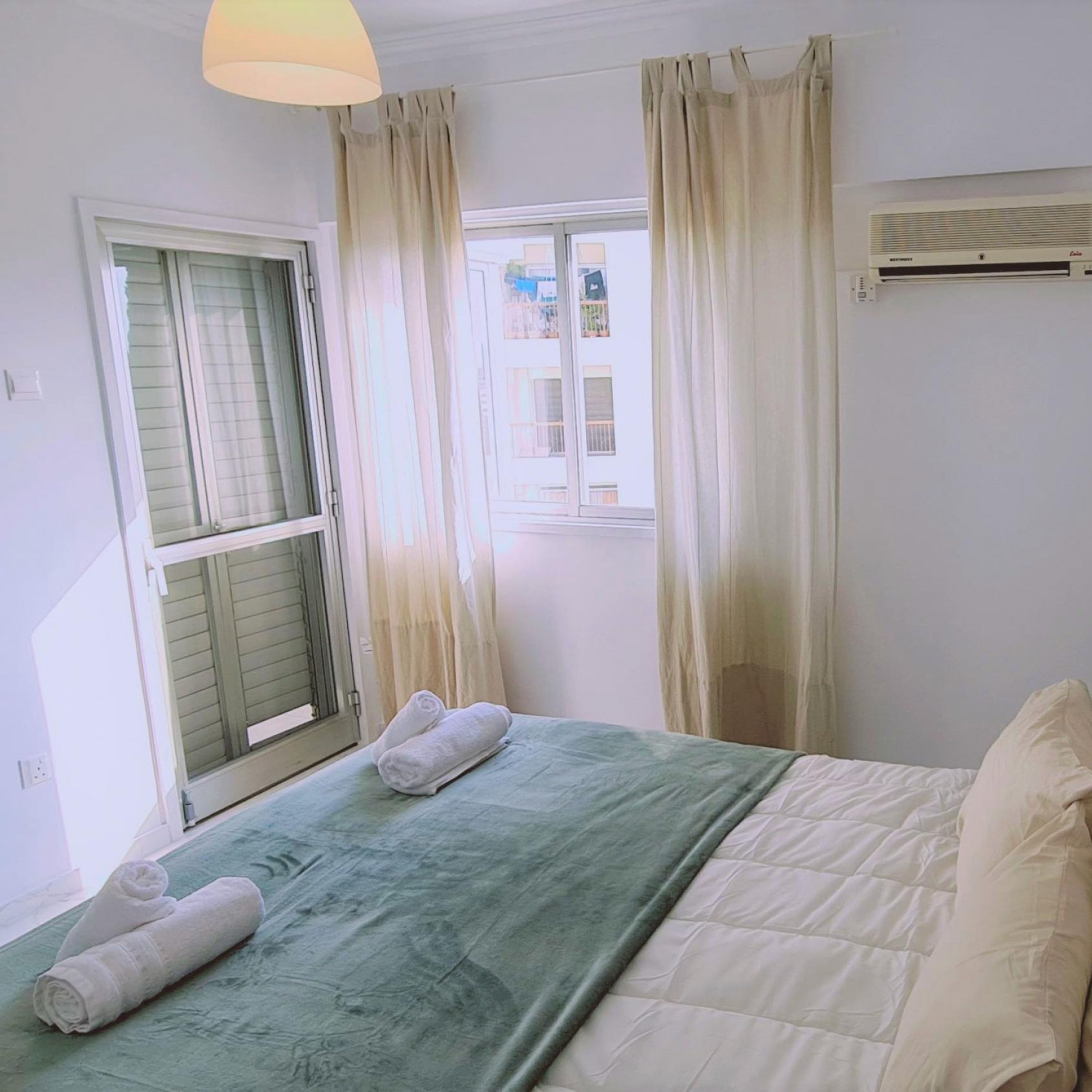 A bedroom with a bed, curtains, a window, and an air conditioning unit.