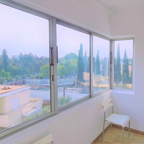 A room with a large window offering a view of trees and a construction site. A white chair is positioned near the window. - 11 EGM - Virtuoso Apartment (Egkomi)