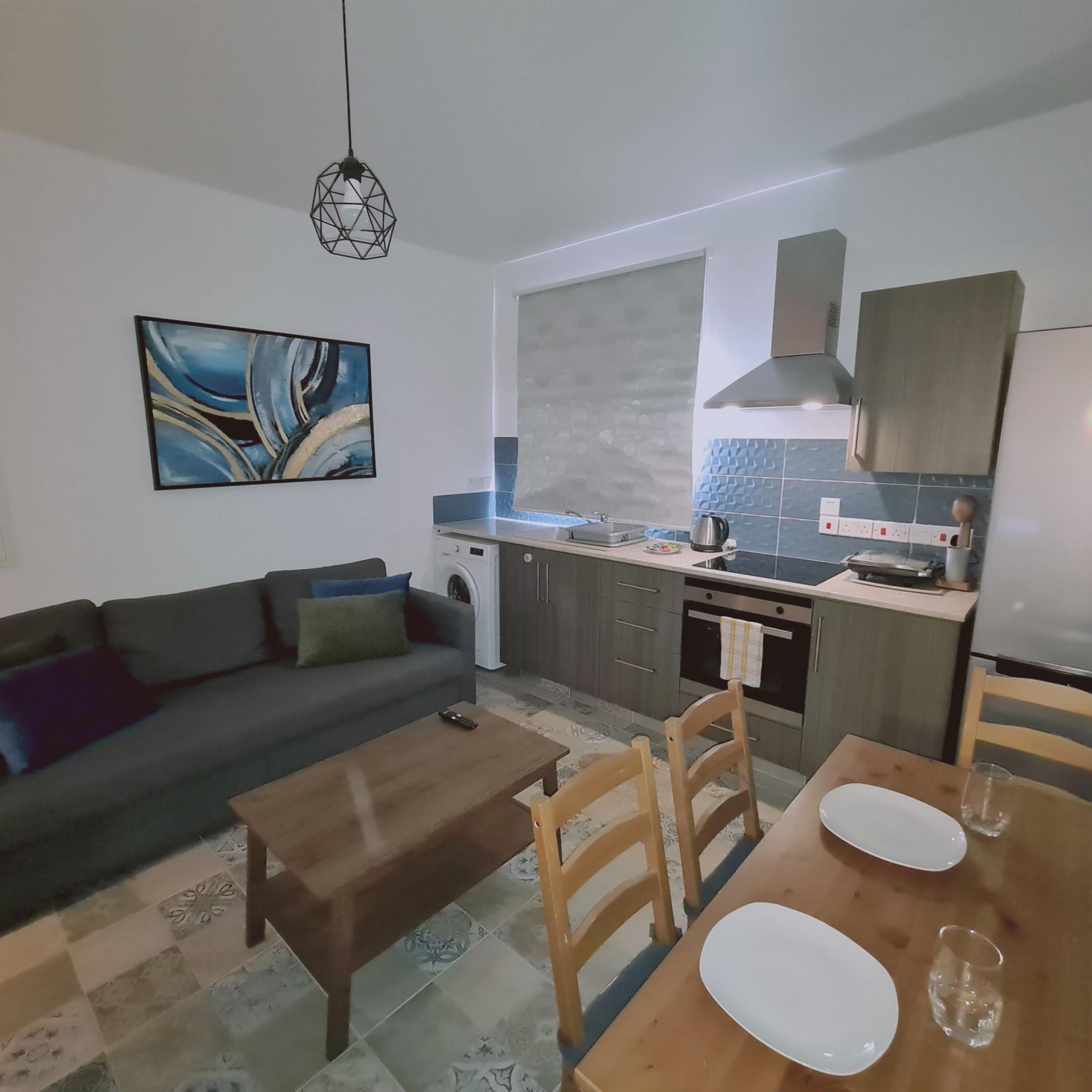 Un salon moderne avec un canapé, une table basse et une table à manger, le tout agrémenté d’assiettes et de verres.