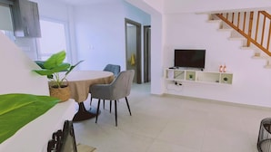 A modern living room with a dining area, a TV, and a staircase. - 48 PER - Mellissa Villa (Paralimni)