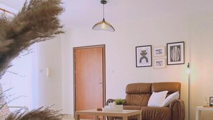 A living room with a brown leather sofa, a wooden coffee table, a small side table, and a floor lamp. There is a door and a wall with framed artwork. - 61 VOR - Sunny Palms (Oroklini)