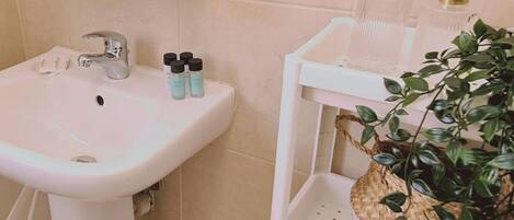 Un baño con lavamanos blanco, un espejo y un estante con artículos de aseo y una planta.