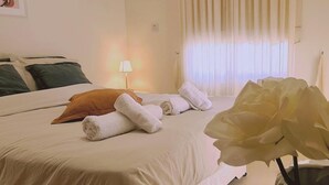A hotel room with a bed, a lamp, a window with curtains, and a vase with a flower. - 61 VOR - Sunny Palms (Oroklini)