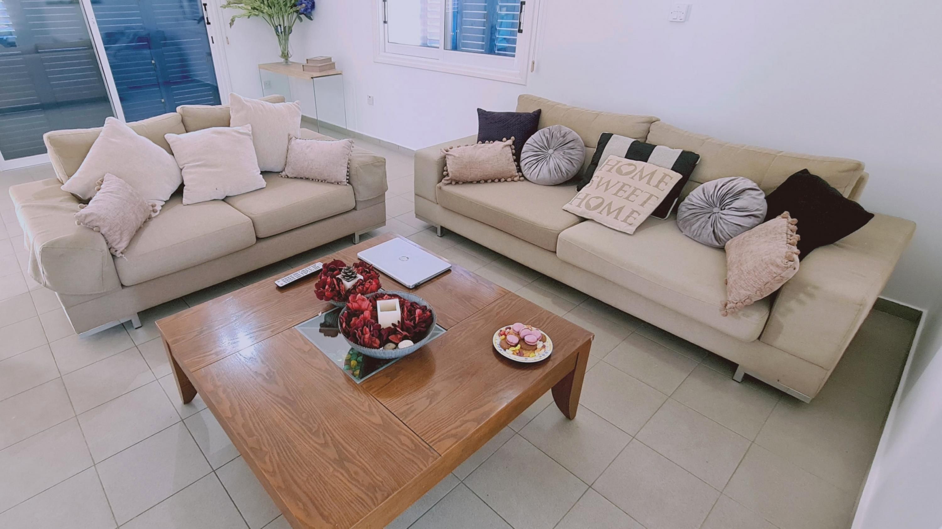 A living room with two beige sofas, a wooden coffee table, and a window with blinds.