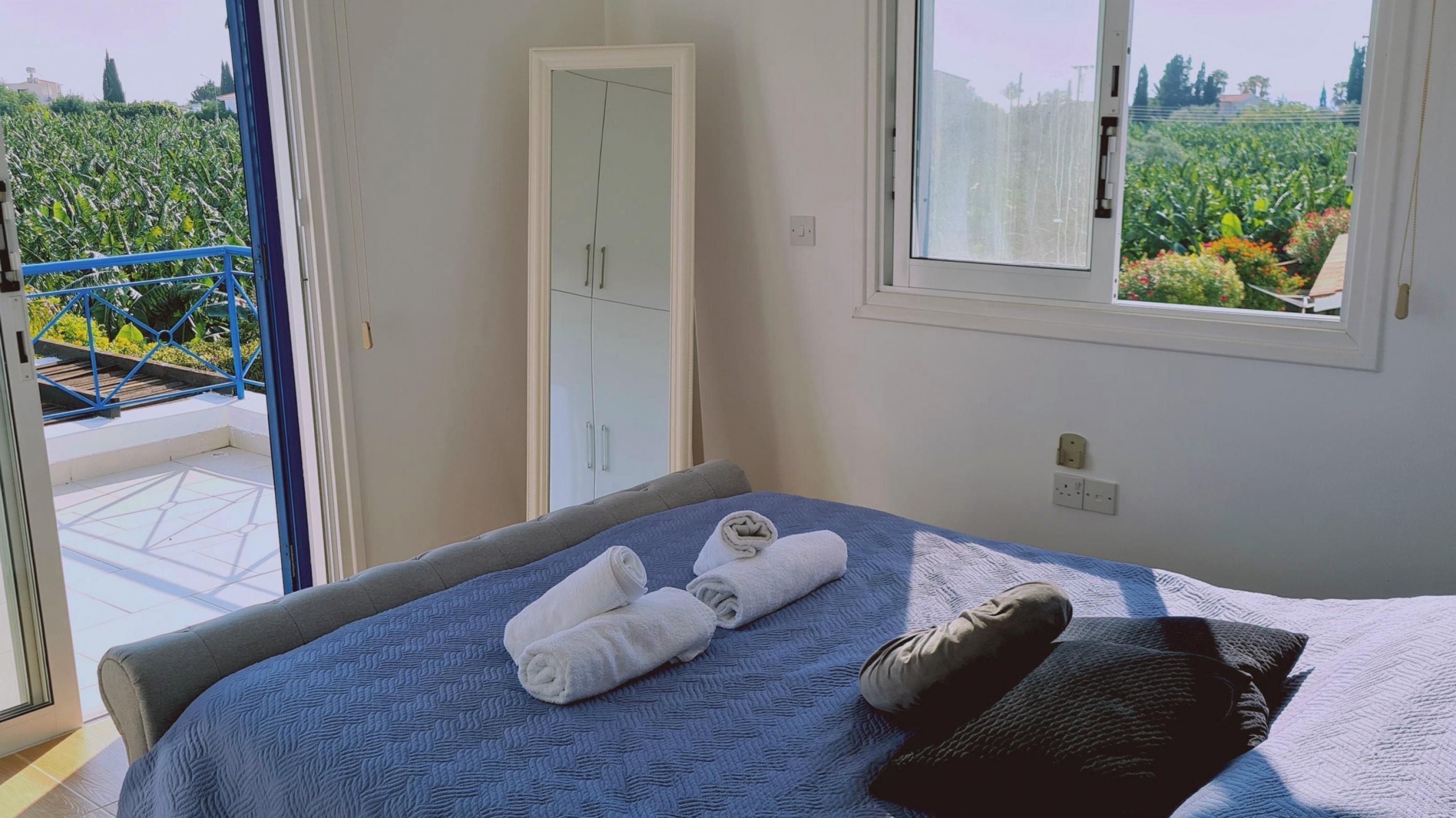 A bedroom with a bed, a window with a view of a garden, and a door leading to a balcony.