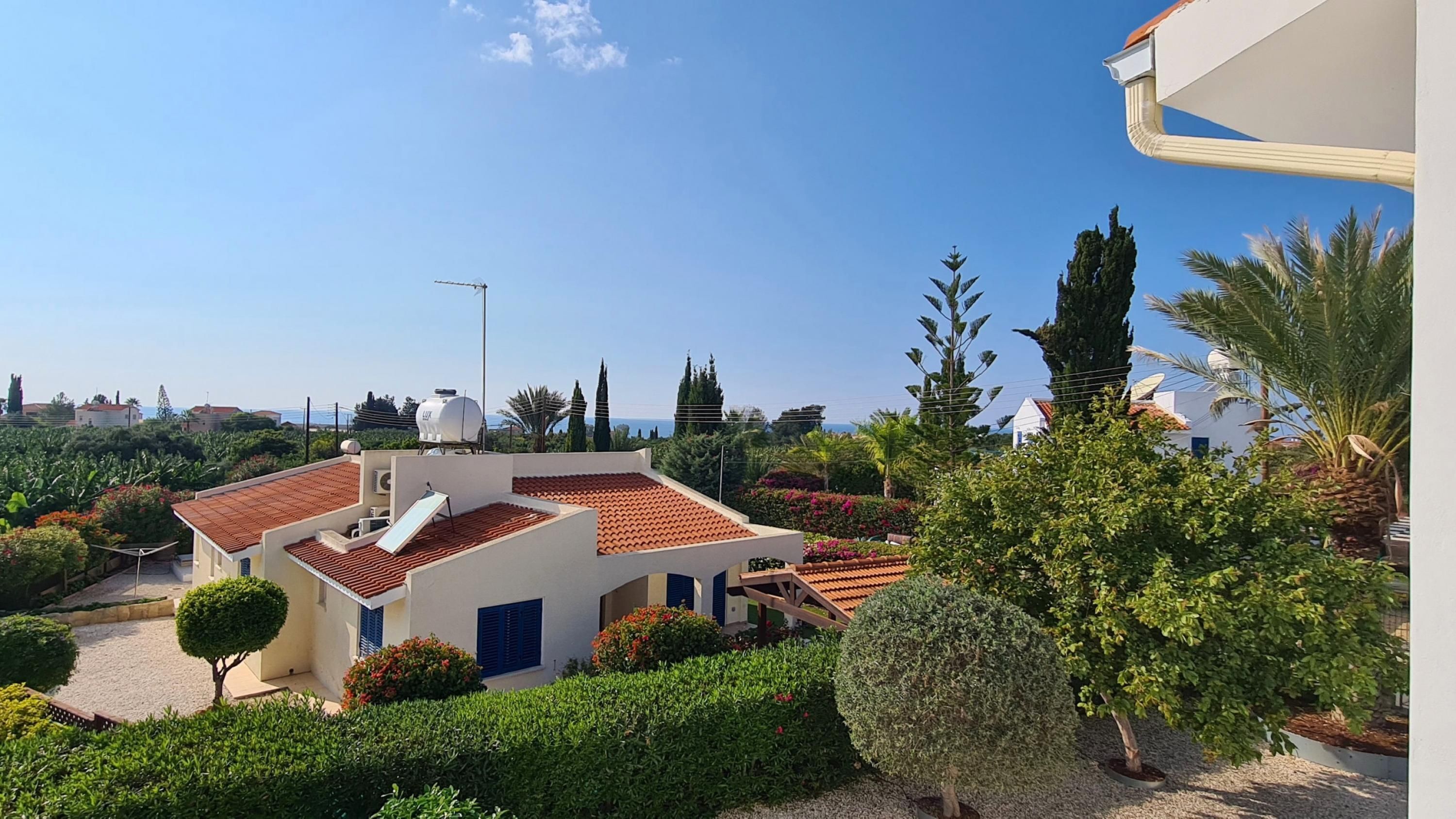 Um edifício residencial com telhado de telhas vermelhas, um reservatório de água e um jardim com diversas plantas e uma pequena árvore.