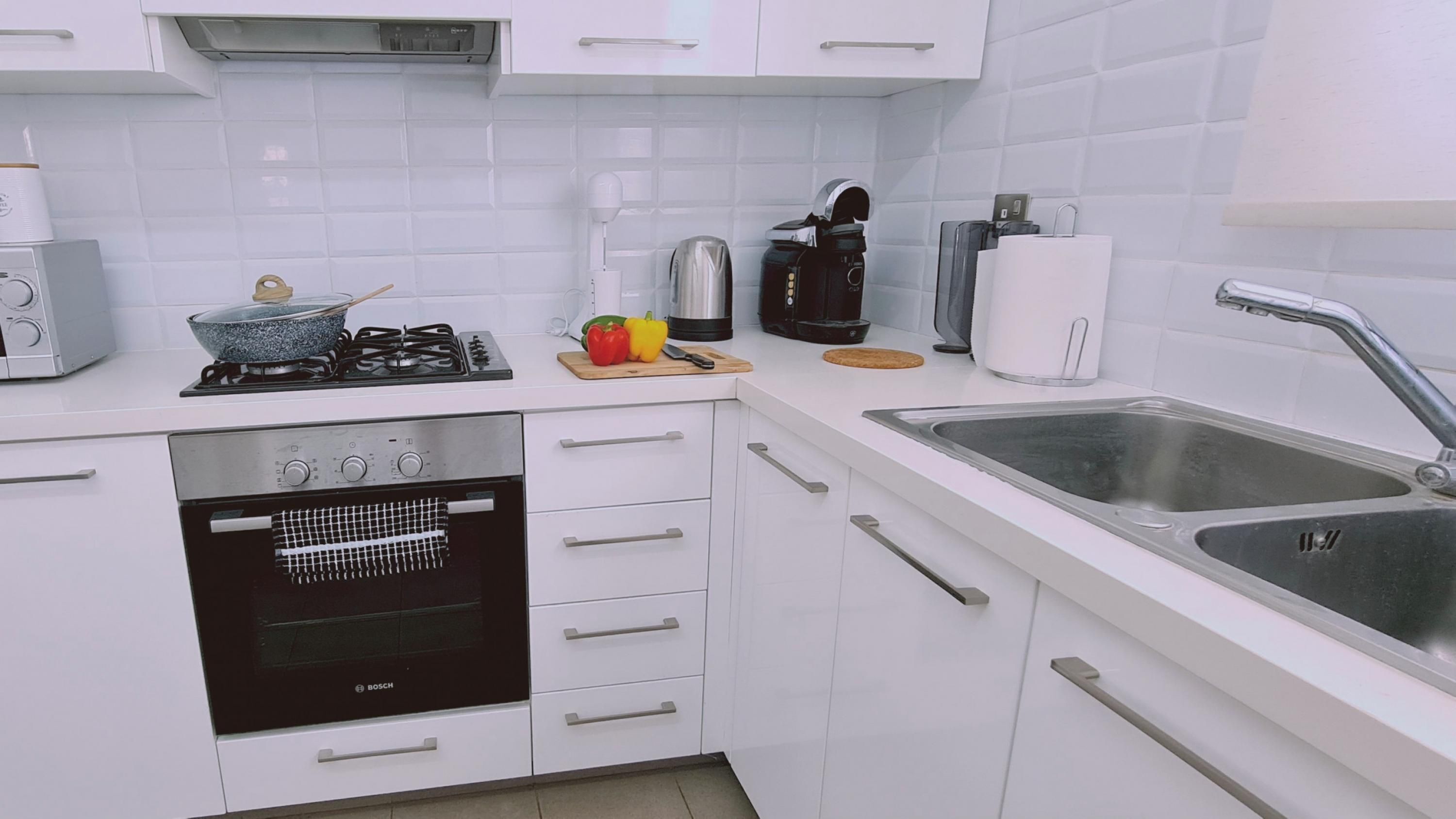 Een moderne keuken met witte kasten, een Bosch oven, een gasfornuis, een spoelbak en diverse apparaten.