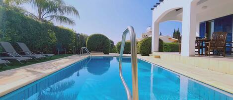A swimming pool with a clear blue water, surrounded by lounge chairs and a modern building with an open patio.