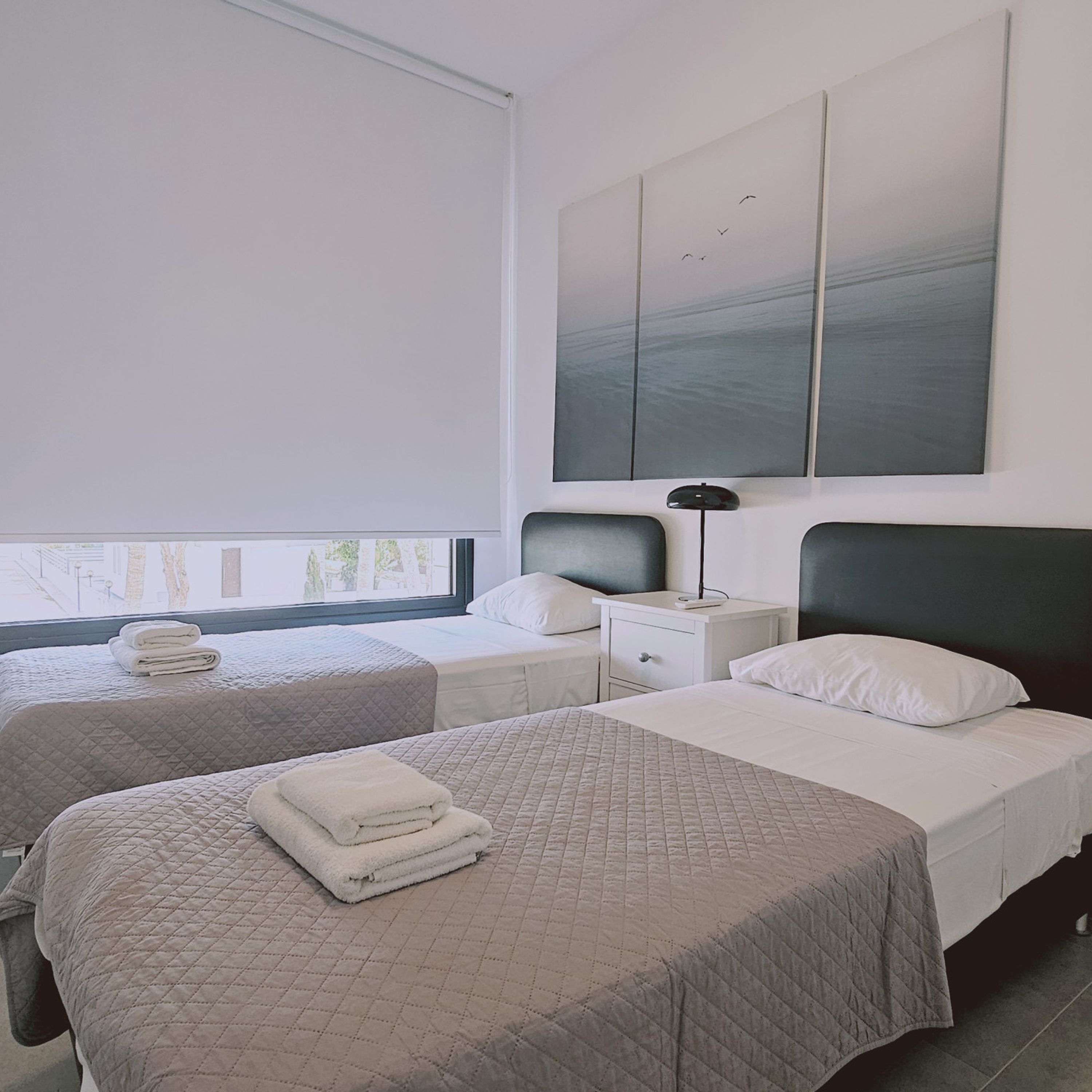 A hotel room with two beds, a large window, a nightstand, and a wall-mounted artwork.